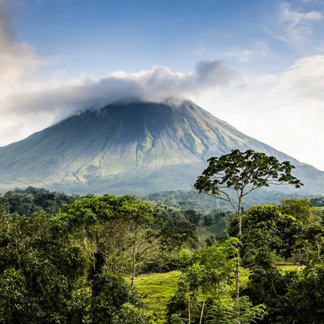 Der Vulkan Arenal erhebt sich kegelförmig über der grünen Landschaft Costa Ricas. Umgeben von Regenwald und Wolken dominiert der markante Vulkan die Szenerie.