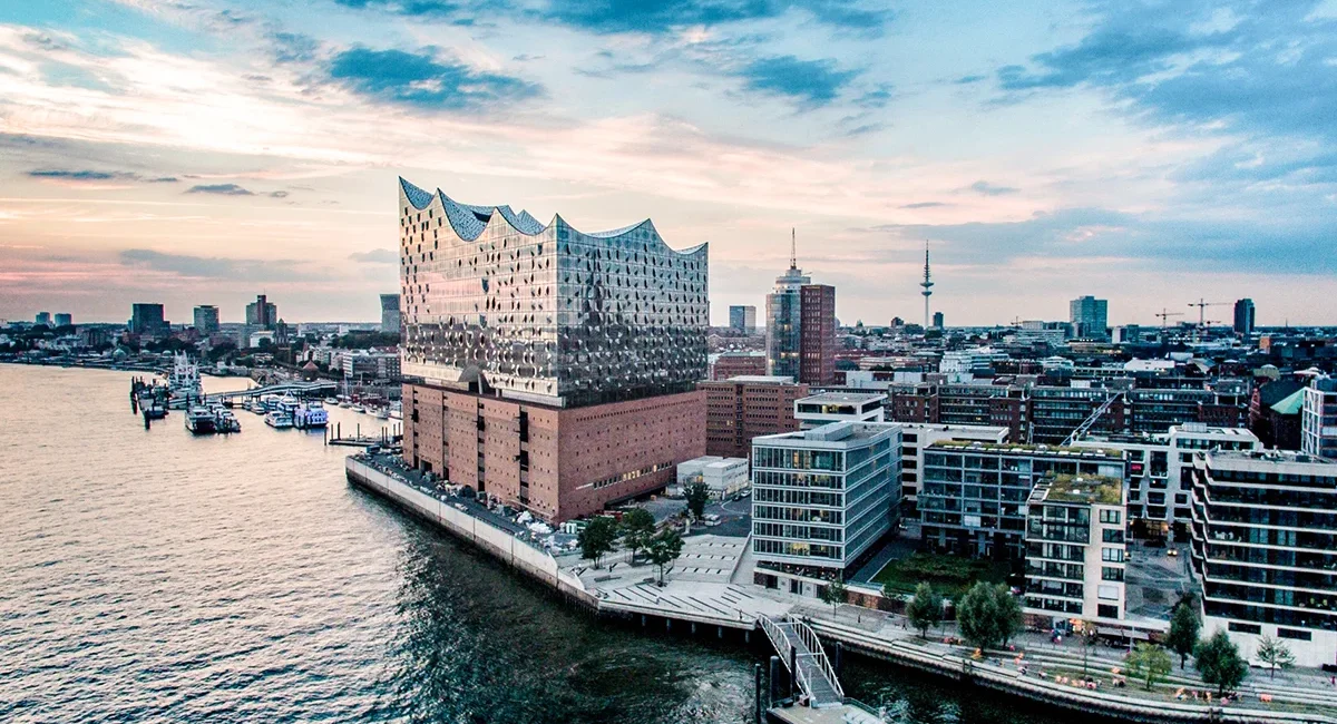 Die Elbphilharmonie in Hamburg steht am Ufer der Elbe. Das moderne Glasgebäude mit wellenförmigem Dach sitzt auf einem historischen Backsteinspeicher im Hafen.