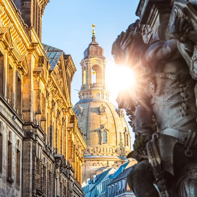 Die historische Münzgasse in Dresden mit Blick auf die markante Kuppel der Dresdner Frauenkirche, die im warmen Licht der tiefstehenden Sonne erstrahlt.