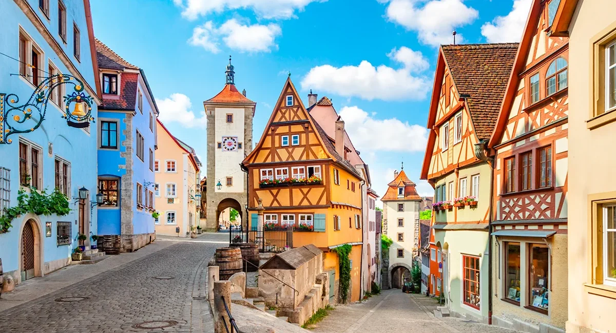 Das Plönlein in Rothenburg ob der Tauber, ein ikonisches gelbes Fachwerkhaus an einer Straßengabelung, das von mittelalterlichen Türmen und Kopfsteinpflaster eingerahmt wird.