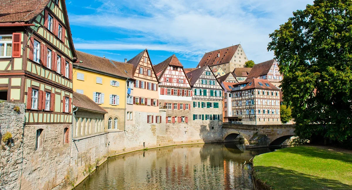 Eine Häuserzeile mit historischen Fachwerkhäusern in der Altstadt von Schwäbisch Hall, die sich im ruhigen Wasser des Flusses Kocher spiegelt.