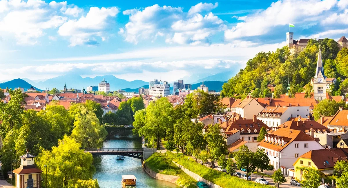 Die malerische Altstadt von Ljubljana am Ufer des Flusses Ljubljanica, über der das historische Schloss auf einem grünen Hügel thront.