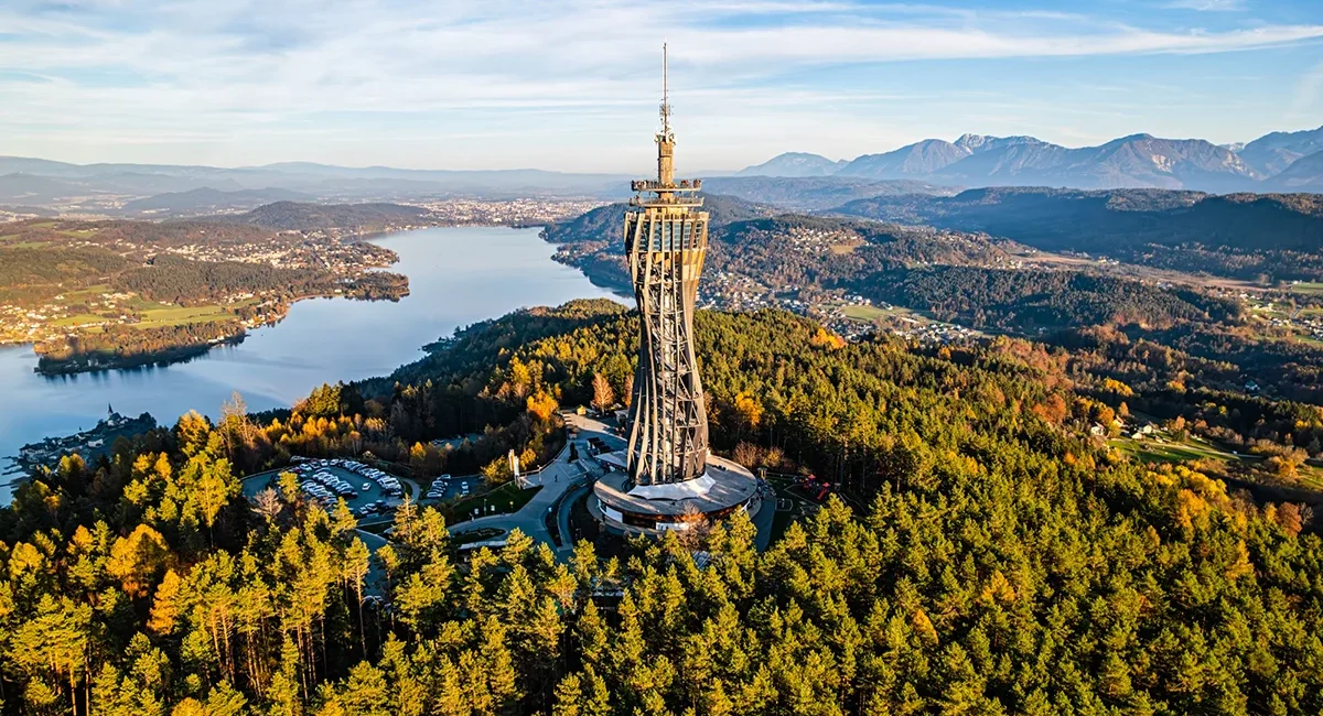 Der Aussichtsturm Pyramidenkogel, der als markante Holzkonstruktion inmitten bewaldeter Hügel über dem glitzernden Wörthersee in Kärnten thront.