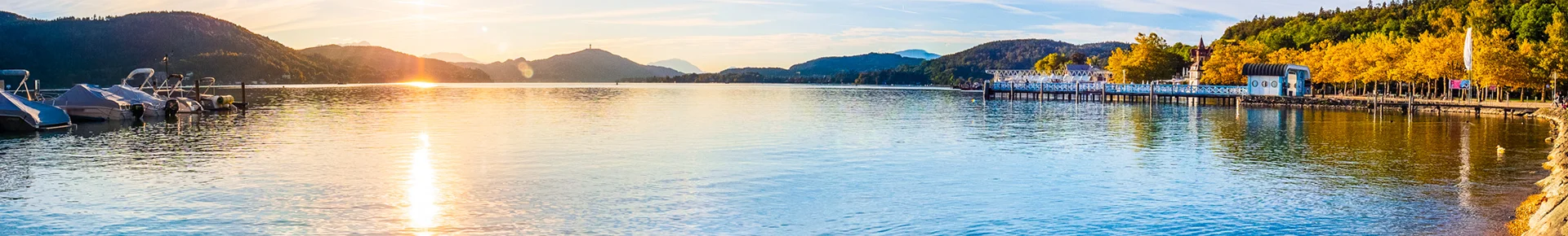 Die herbstliche Ostbucht des Wörthersees in Klagenfurt bei Sonnenuntergang, mit Blick über das ruhige Wasser auf die Kärntner Hügellandschaft.