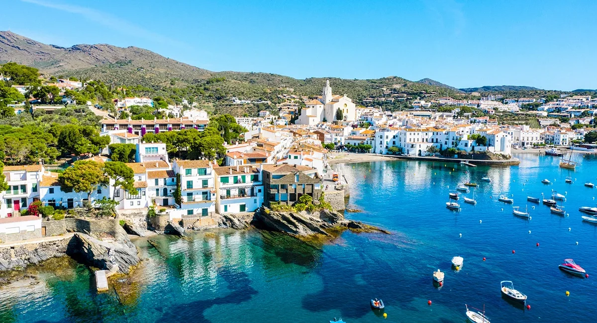Das Küstendorf Cadaqués in Katalonien mit weißen Häusern am Meer und Booten im Hafen.