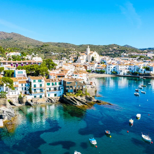 Das Küstendorf Cadaqués in Katalonien mit weißen Häusern am Meer und Booten im Hafen.