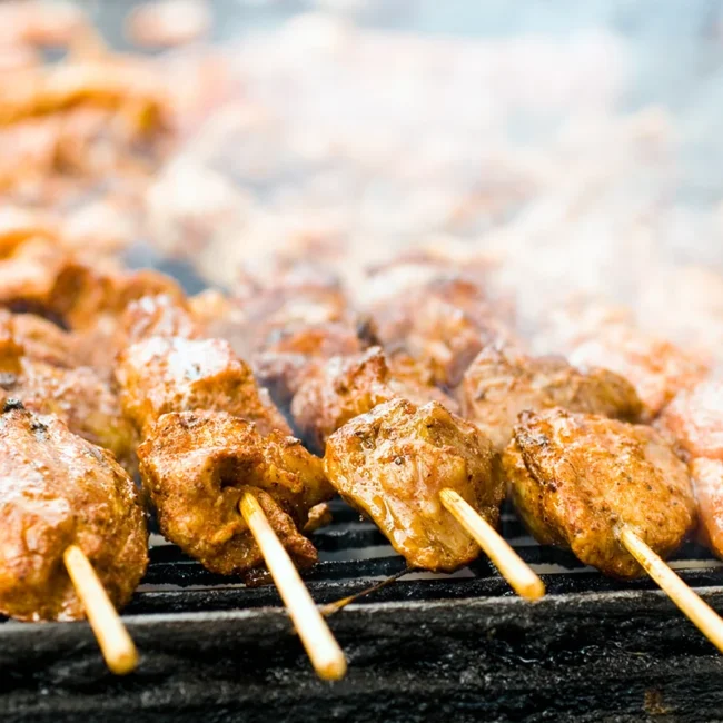 Ein Espetada-Rindfleischspieß wird auf einem Grill zubereitet. Die Fleischstücke stecken auf einem langen Spieß über der heißen Glut.