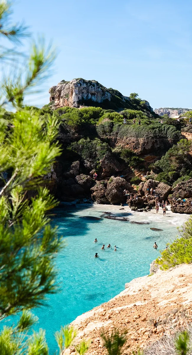 Eine Bucht auf Mallorca mit türkisfarbenem Wasser, umgeben von Felsen und einer kleinen Strandfläche.