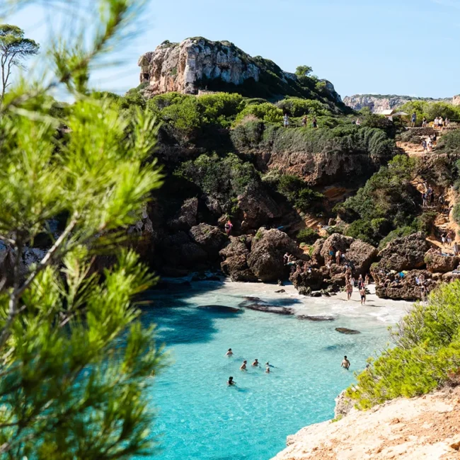 Eine Bucht auf Mallorca mit türkisfarbenem Wasser, umgeben von Felsen und einer kleinen Strandfläche.