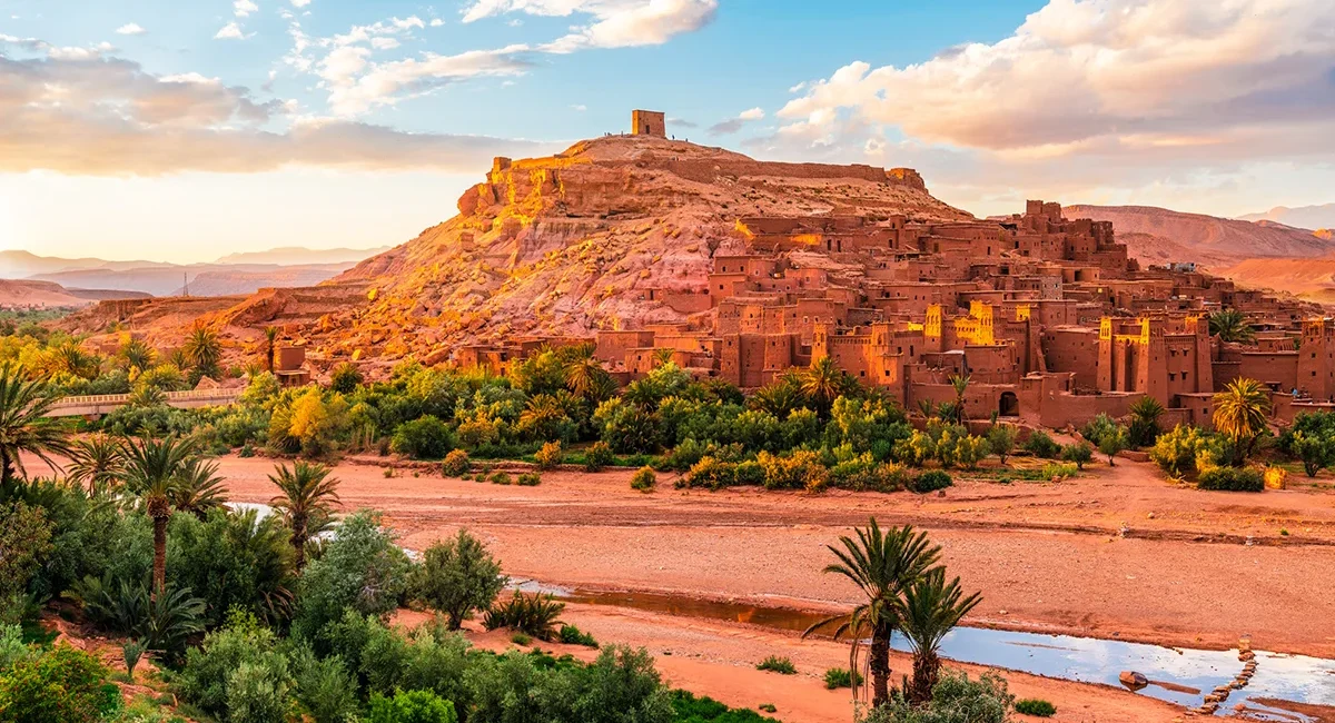 Die Wüstenstadt Ait Benhaddou in Marokko besteht aus traditionellen Lehmhäusern, die sich an einem Hügel in der trockenen Landschaft entlangziehen.