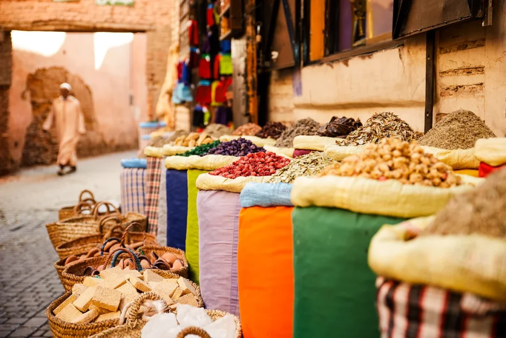 Bunte Gewürze sind in großen Haufen auf einem Marktstand im Souk von Marrakesch ausgestellt. Die verschiedenen Farben und Formen der Gewürze prägen das lebhafte Marktbild.