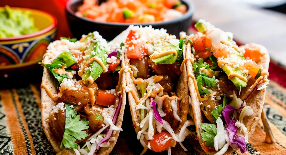 Drei Tacos liegen auf einem Teller. Die gefüllten Tortillas sind mit verschiedenen Zutaten belegt und typisch für die mexikanische Küche.
