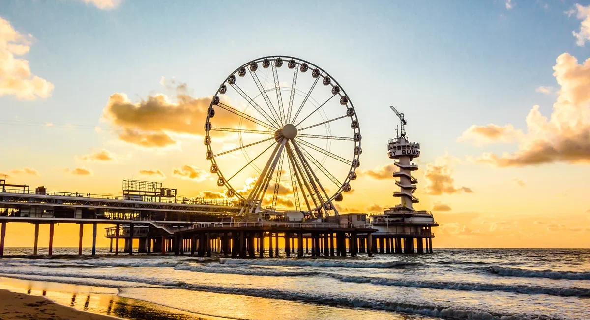 Der Pier von Scheveningen ragt ins Meer hinaus. Am Ende des Piers steht ein großes Riesenrad über der Nordsee.