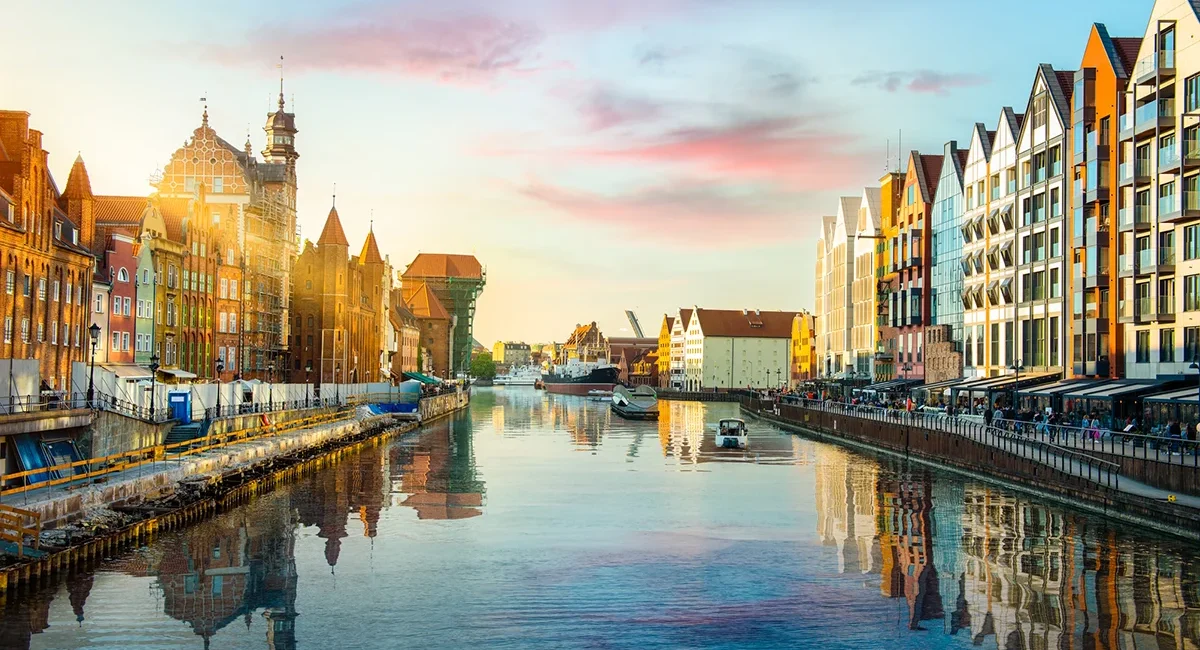 Die Altstadt von Danzig mit historischen Häusern am Hafen entlang der Mottlau. Bunte Fassaden spiegeln sich im Wasser des Hafens.