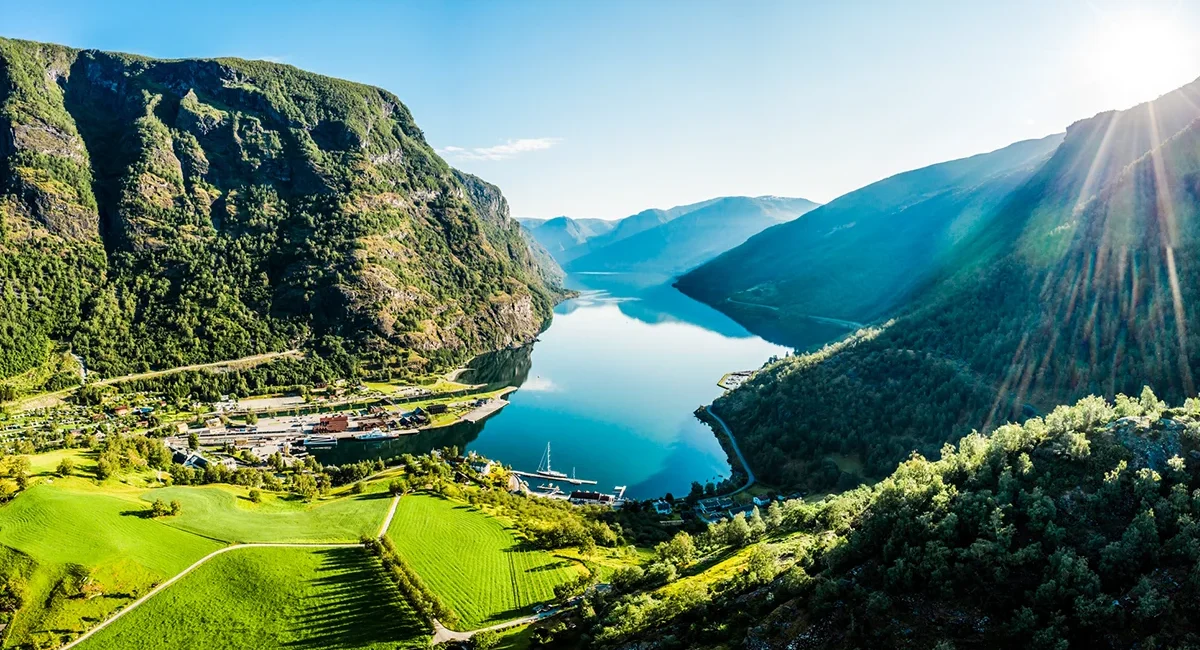 Der Aurlandsfjord in Norwegen liegt im Sonnenschein zwischen hohen Bergen. Das ruhige Wasser des Fjords spiegelt die umliegende Landschaft.