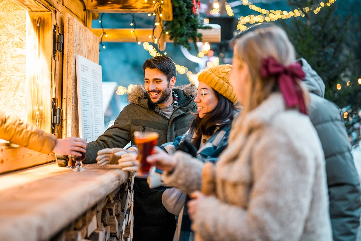 Gruppe junger Menschen bestellt Glühwein an einem Stand auf dem Weihnachtsmarkt