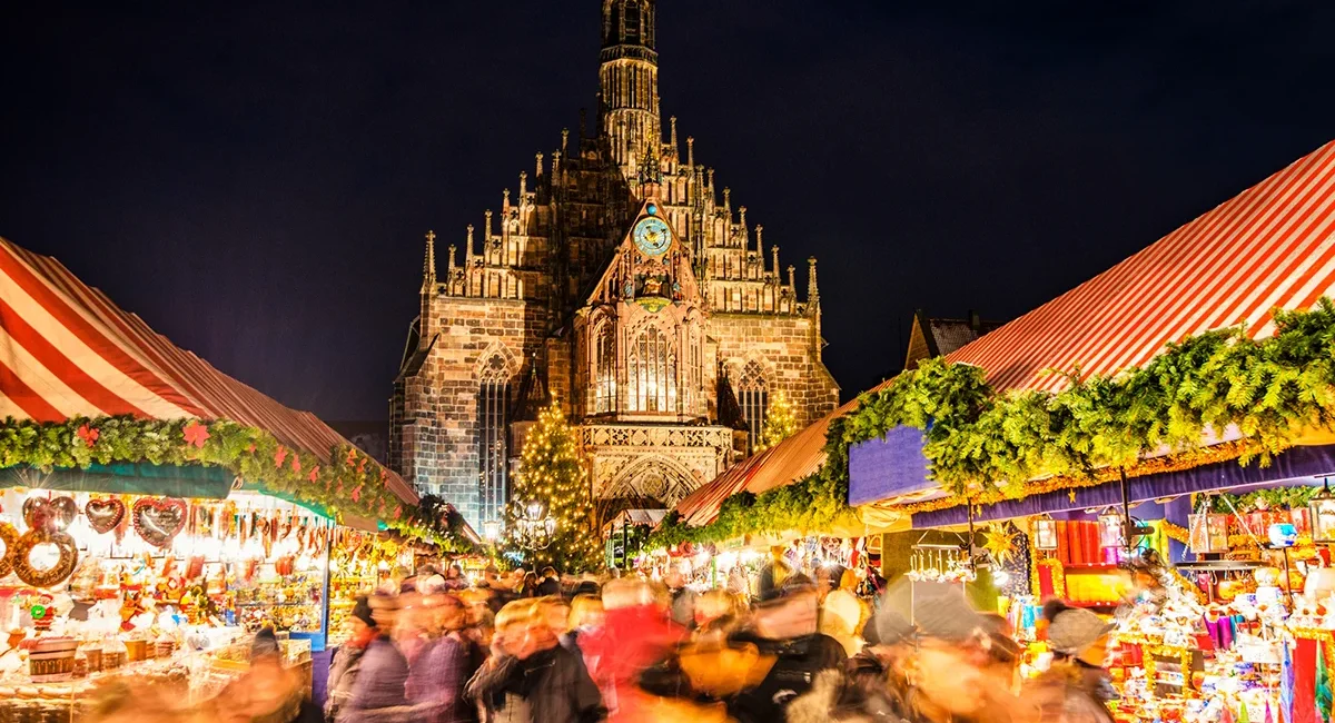 Blick über den Nürnberger Weihnachtsmarkt auf eine beleuchtete Kirche im Hintergrund