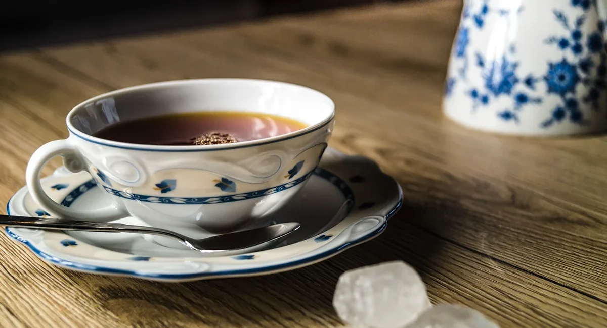 Eine traditionelle ostfriesische Teezeremonie mit einer gefüllten Porzellantasse, einem Teelöffel und charakteristischen Kluntjes auf einem rustikalen Holztisch.