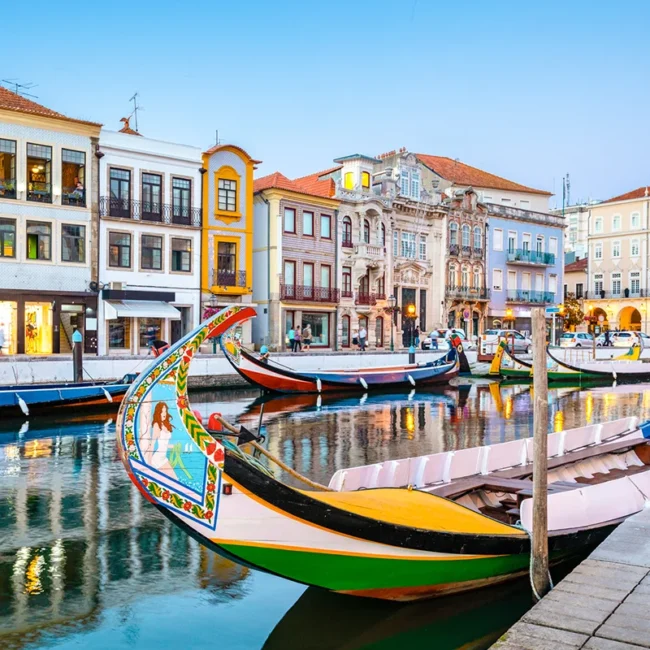 Bunte Moliceiro-Boote fahren durch einen Kanal in Aveiro in Portugal. Die traditionellen Boote liegen auf dem Wasser zwischen Häusern am Ufer.