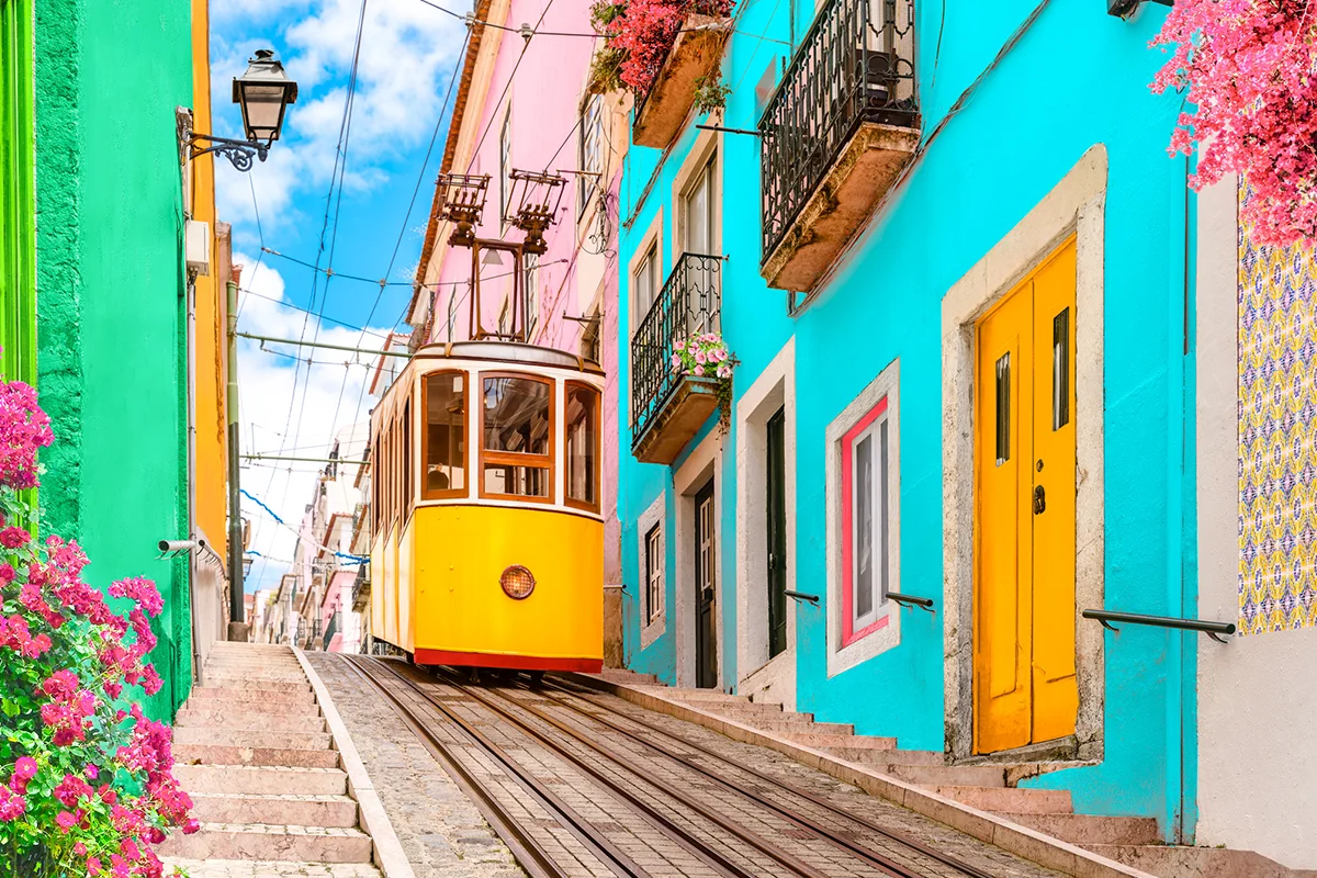 Eine gelbe Straßenbahn fährt durch eine enge Straße mit bunten Häusern in Lissabon. Die historische Tram ist typisch für das Stadtbild der portugiesischen Hauptstadt.