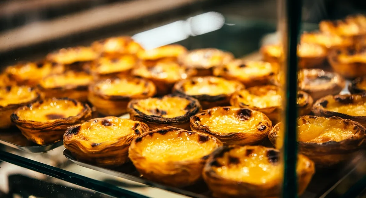 Mehrere Pastéis de Nata liegen in einer Auslage einer Bäckerei. Die kleinen portugiesischen Blätterteigtörtchen sind mit goldbrauner Vanillecreme gefüllt.