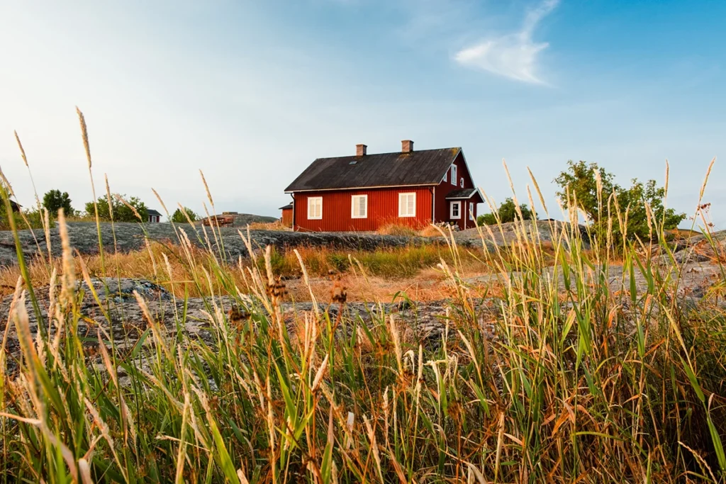 Ein typisches rotes Holzhaus steht in der Landschaft Schwedens. Das Haus ist von Wiesen und Natur umgeben.