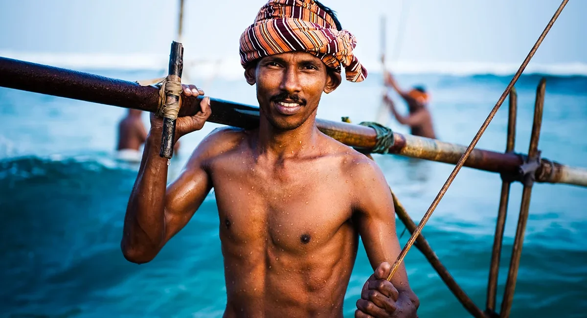 Ein Fischer steht oberkörperfrei im Meer vor der Küste von Sri Lanka und ist beim Fischen im Wasser.