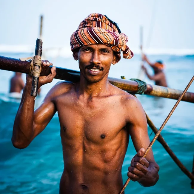 Ein Fischer steht oberkörperfrei im Meer vor der Küste von Sri Lanka und ist beim Fischen im Wasser.
