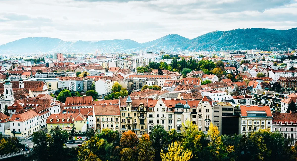 Blick über die Stadt Graz mit vielen roten Dächern und historischen Gebäuden. Die Altstadt erstreckt sich zwischen Hügeln in der Steiermark.