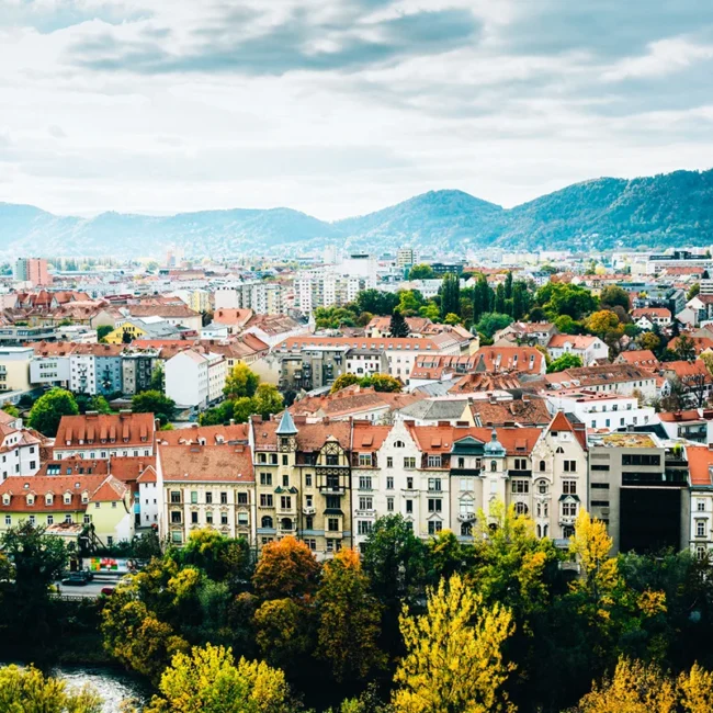 Blick über die Stadt Graz mit vielen roten Dächern und historischen Gebäuden. Die Altstadt erstreckt sich zwischen Hügeln in der Steiermark.