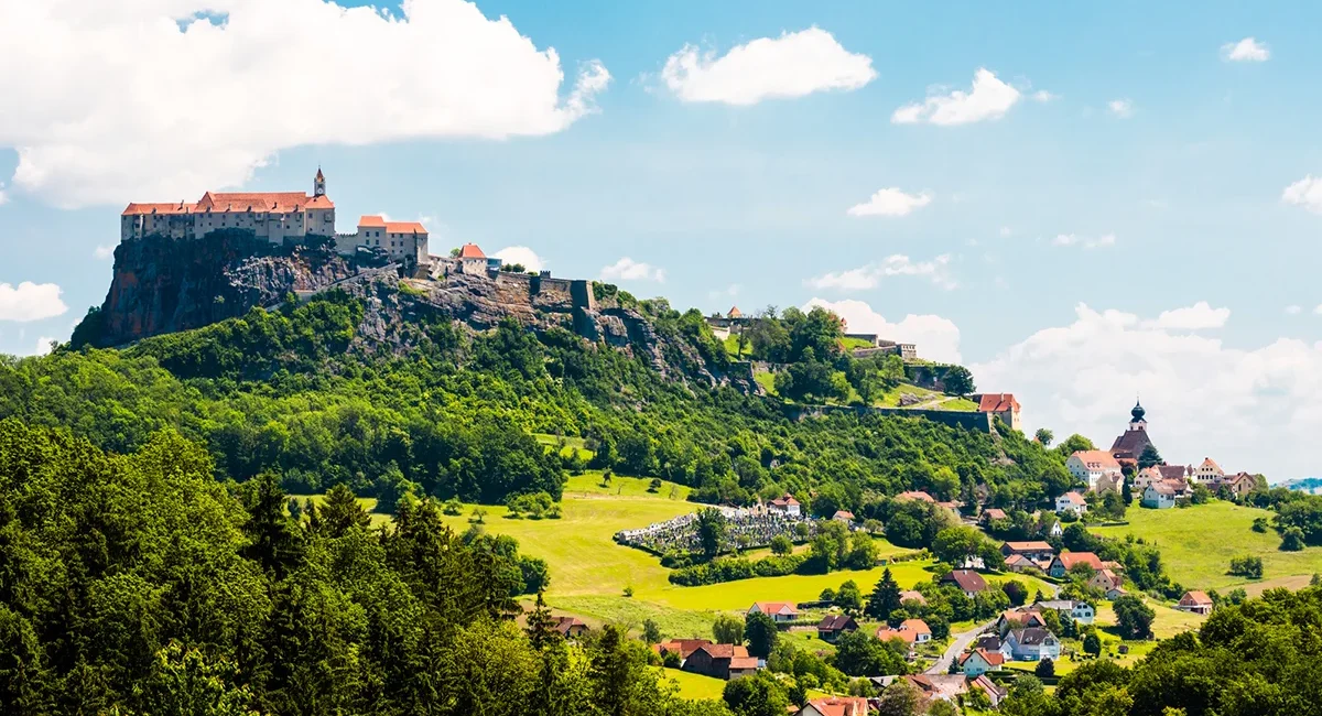 Die Riegersburg in der Steiermark thront auf einem steilen Felsen über der umliegenden Landschaft. Die historische Burganlage ist von grünen Hügeln umgeben.