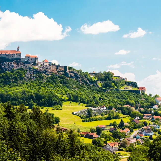 Die Riegersburg in der Steiermark thront auf einem steilen Felsen über der umliegenden Landschaft. Die historische Burganlage ist von grünen Hügeln umgeben.