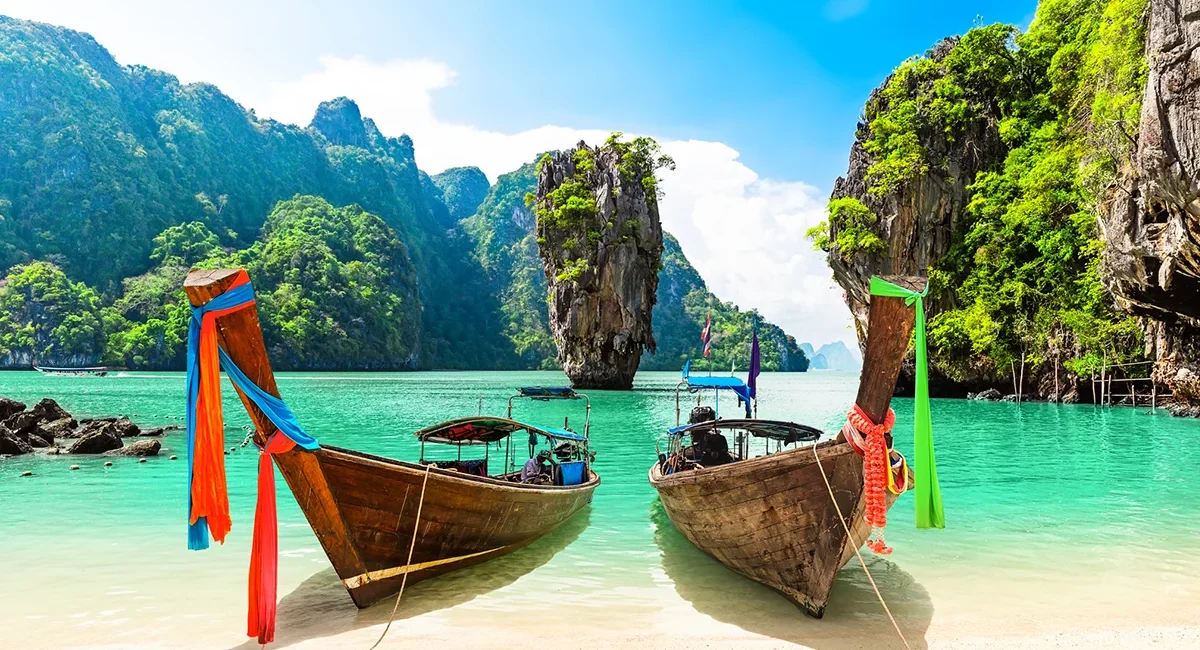 Ein typischer Strand auf Phuket in Thailand mit traditionellen Booten im türkisfarbenen Wasser.