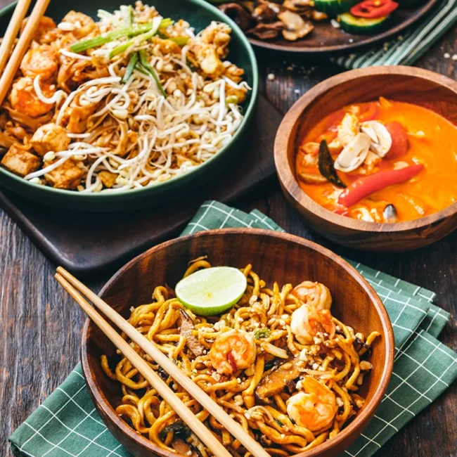 Ein thailändisches Gericht mit Reisnudeln und Curry, angerichtet in einer Schale mit verschiedenen Zutaten.