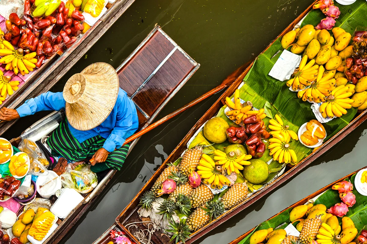 Vogelperspektive auf einen schwimmenden Markt in Thailand mit vielen Booten auf einem Kanal.