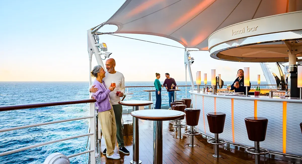 Auf der Lanai Bar auf dem AIDA-Schiff stehen zwei Paare auf dem Deck und trinken entspannt ihre Getränke.