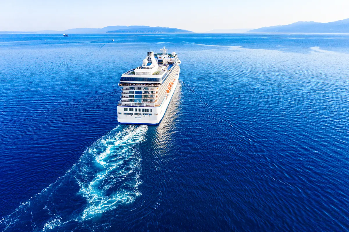 Ein großes Kreuzfahrtschiff fährt über das offene Mittelmeer. In der Ferne ist die Küste mit Land in Sicht.