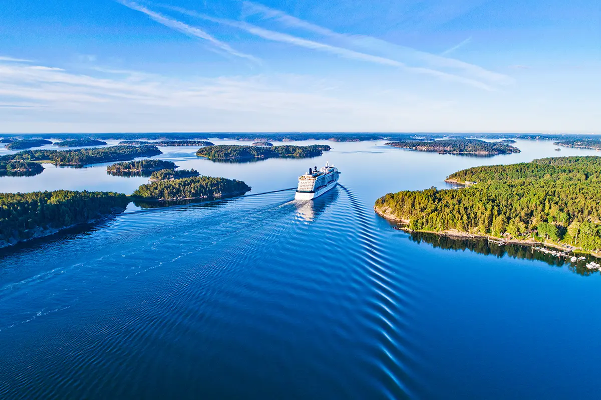 Ein großes Kreuzfahrtschiff fährt durch die schwedischen Schären zwischen kleinen Inseln und Felsen.