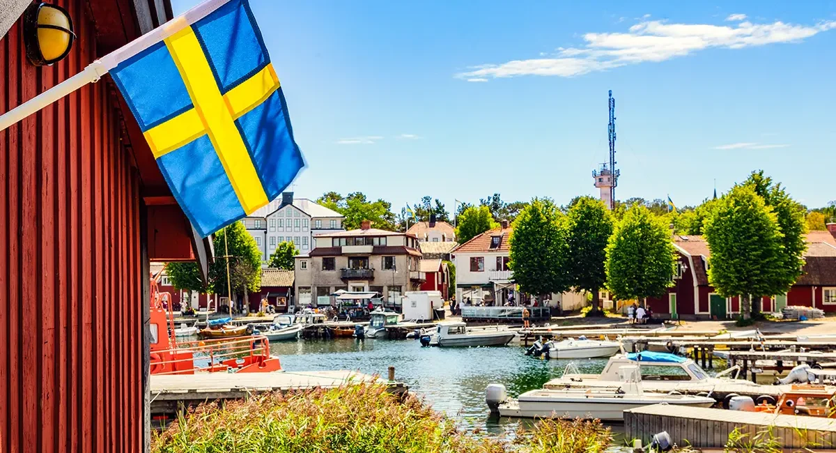 Ein kleiner Hafen in Schweden mit einem roten Schuppen am Wasser und einer schwedischen Flagge.