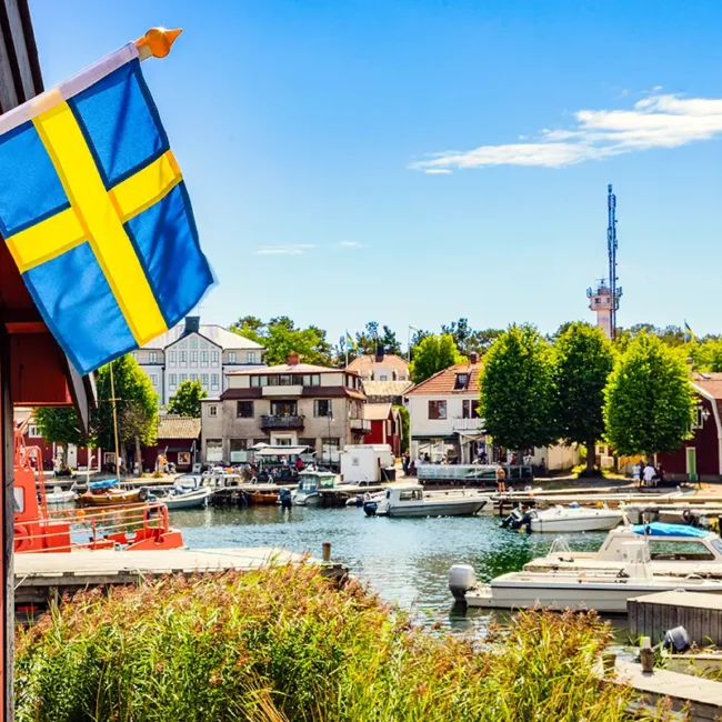 Ein kleiner Hafen in Schweden mit einem roten Schuppen am Wasser und einer schwedischen Flagge.