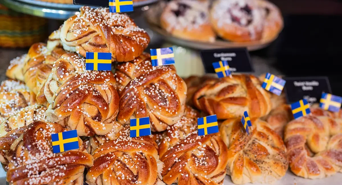 Mehrere schwedische Zimtschnecken liegen in der Auslage eines Cafés, dekoriert mit einer kleinen schwedischen Flagge.