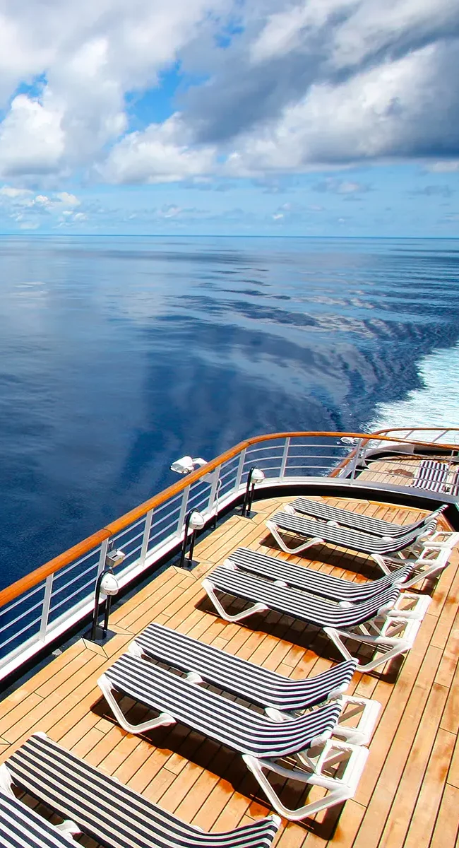 Auf der Sonnenterrasse eines AIDA-Kreuzfahrtschiffs stehen mehrere Liegestühle mit freiem Blick auf das offene Meer.