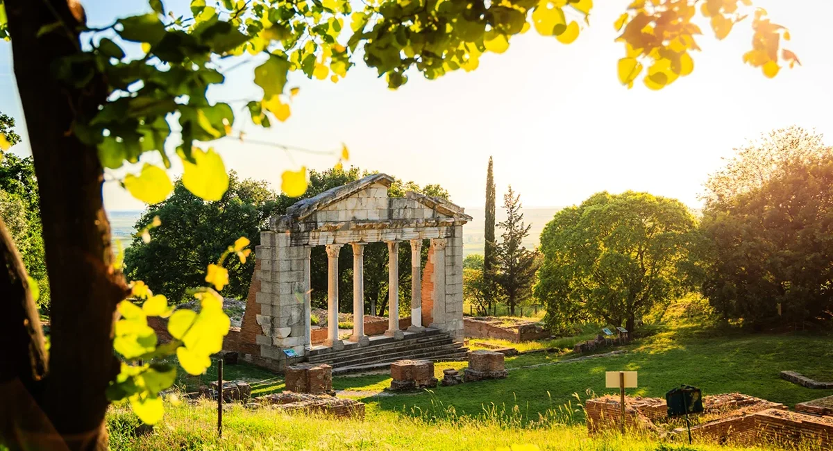 Die sonnendurchfluteten Ruinen des antiken Bouleuterions im Archäologischen Park Apollonia in Albanien, umgeben von grüner Landschaft.