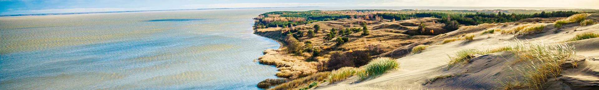 Die weite, sandige Dünenlandschaft des Naturschutzgebiets Nagliai auf der Kurischen Nehrung im Baltikum, die direkt an das ruhige Wasser des Kurischen Haffs grenzt.