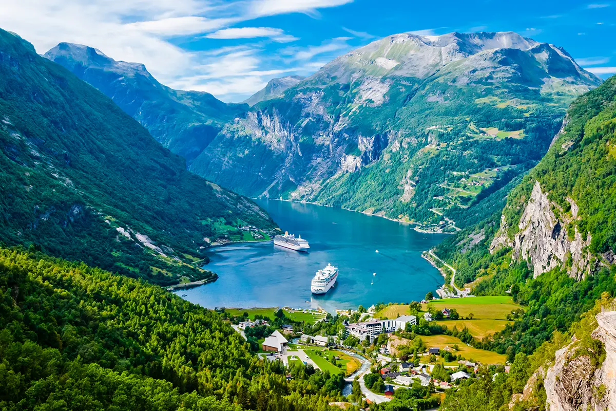 Mehrere Kreuzfahrtschiffe fahren durch einen norwegischen Fjord zwischen hohen Bergen.