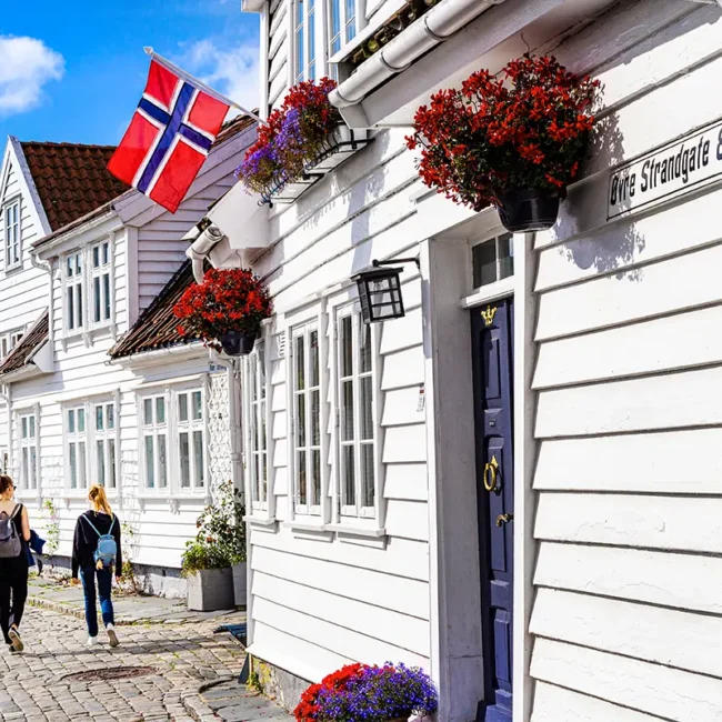 Eine Gasse in Stavanger mit weißen Holzhäusern, Blumentöpfen und einer norwegischen Flagge.