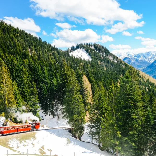 Die rote Schafbergbahn fährt durch eine winterliche Berglandschaft auf den Schafberg am Wolfangssee in Österreich