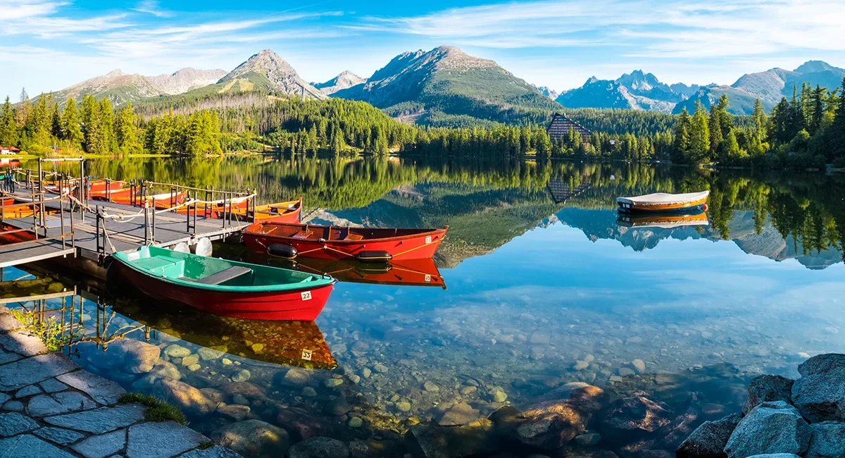 Blick auf einen Bergsee im hohen Tatra Gebirge in der Slowakei. Auf dem klaren See spiegeln sich die kleinen roten Fischerboote