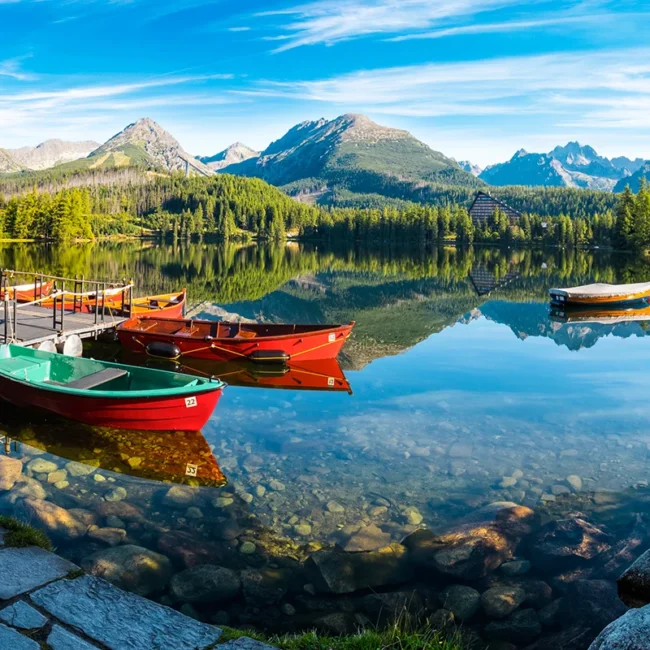 Blick auf einen Bergsee im hohen Tatra Gebirge in der Slowakei. Auf dem klaren See spiegeln sich die kleinen roten Fischerboote