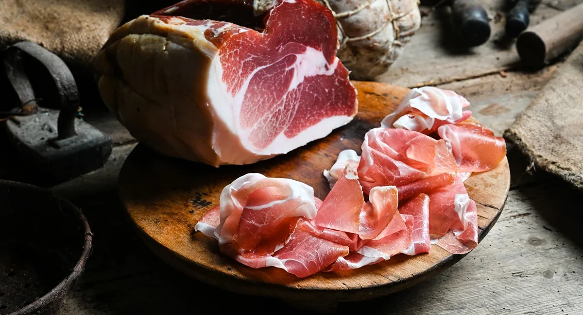 Dünn geschnittener Prosciutto liegt auf einer Holzplatte angerichtet.